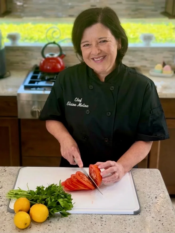 Elaine cortando tomates, con perejil y limones a mano